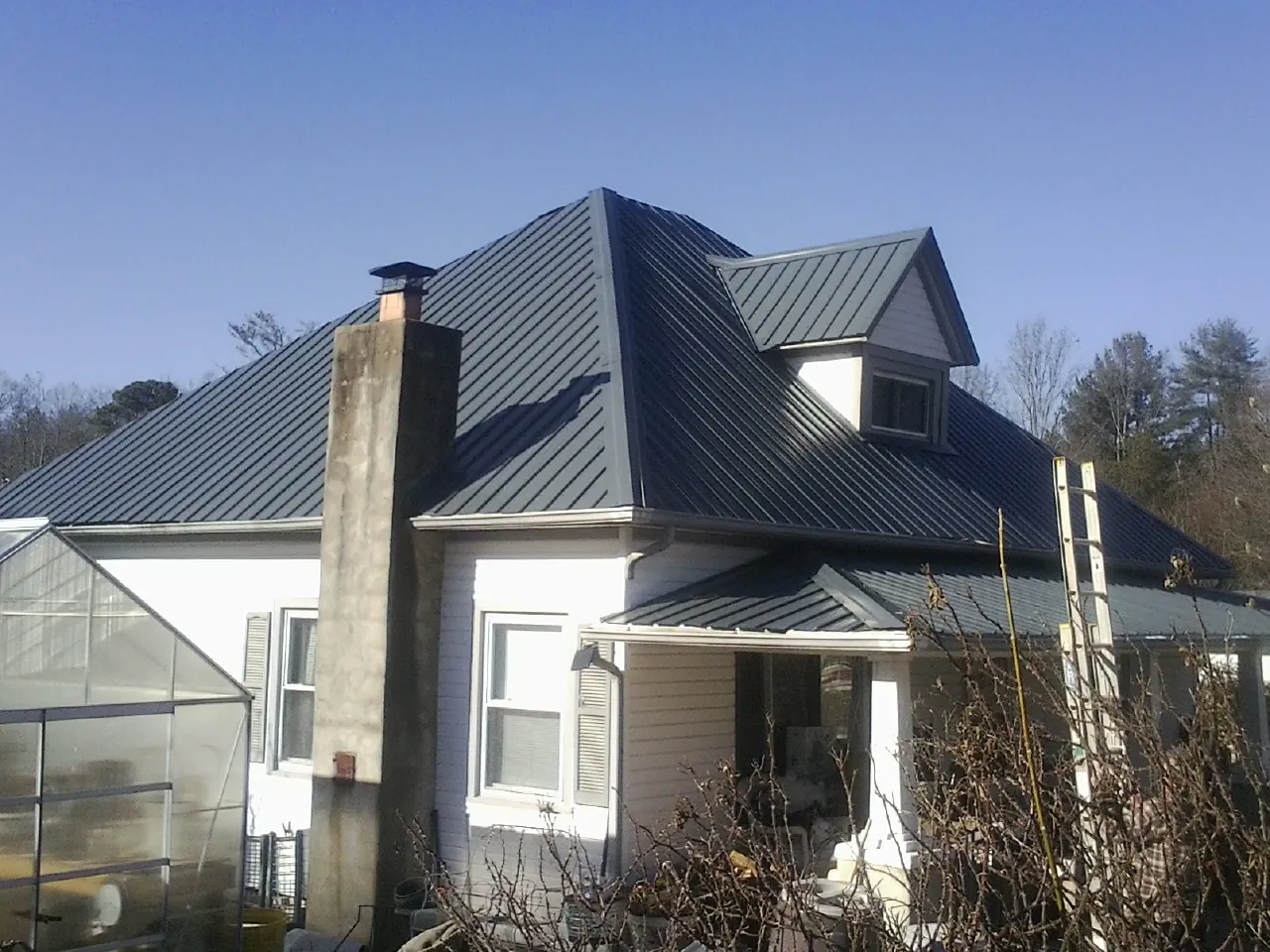 Dark blue standing seam metal roof on a white farmhouse with dormer — Slate & Tile Roof Repair by Roofing Brothers in Alcoa
