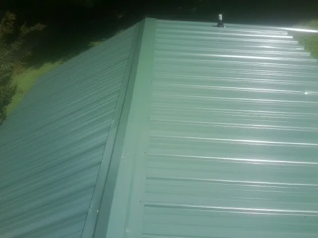 New green metal panels meeting at the ridge of a roof — Flat Roof Repair work by our crew in Alcoa