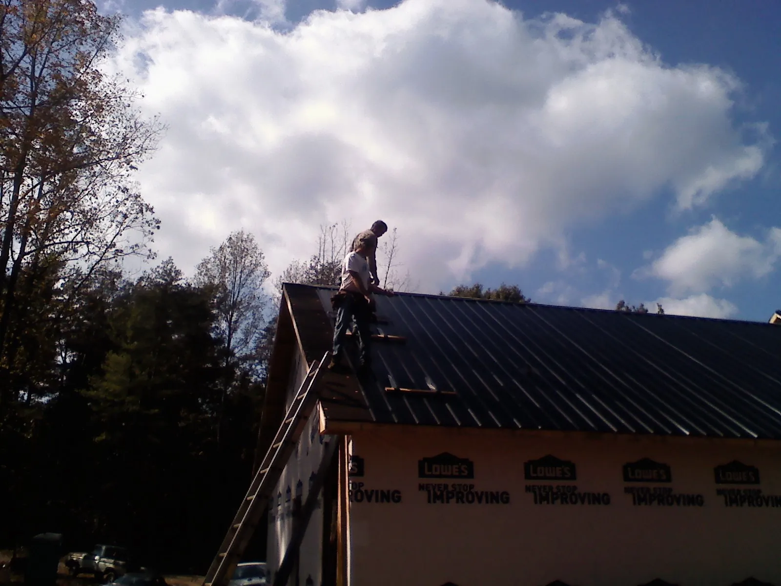 Roofer fastening dark metal panels high against a cloudy sky, from a Roof Inspection job in Alcoa