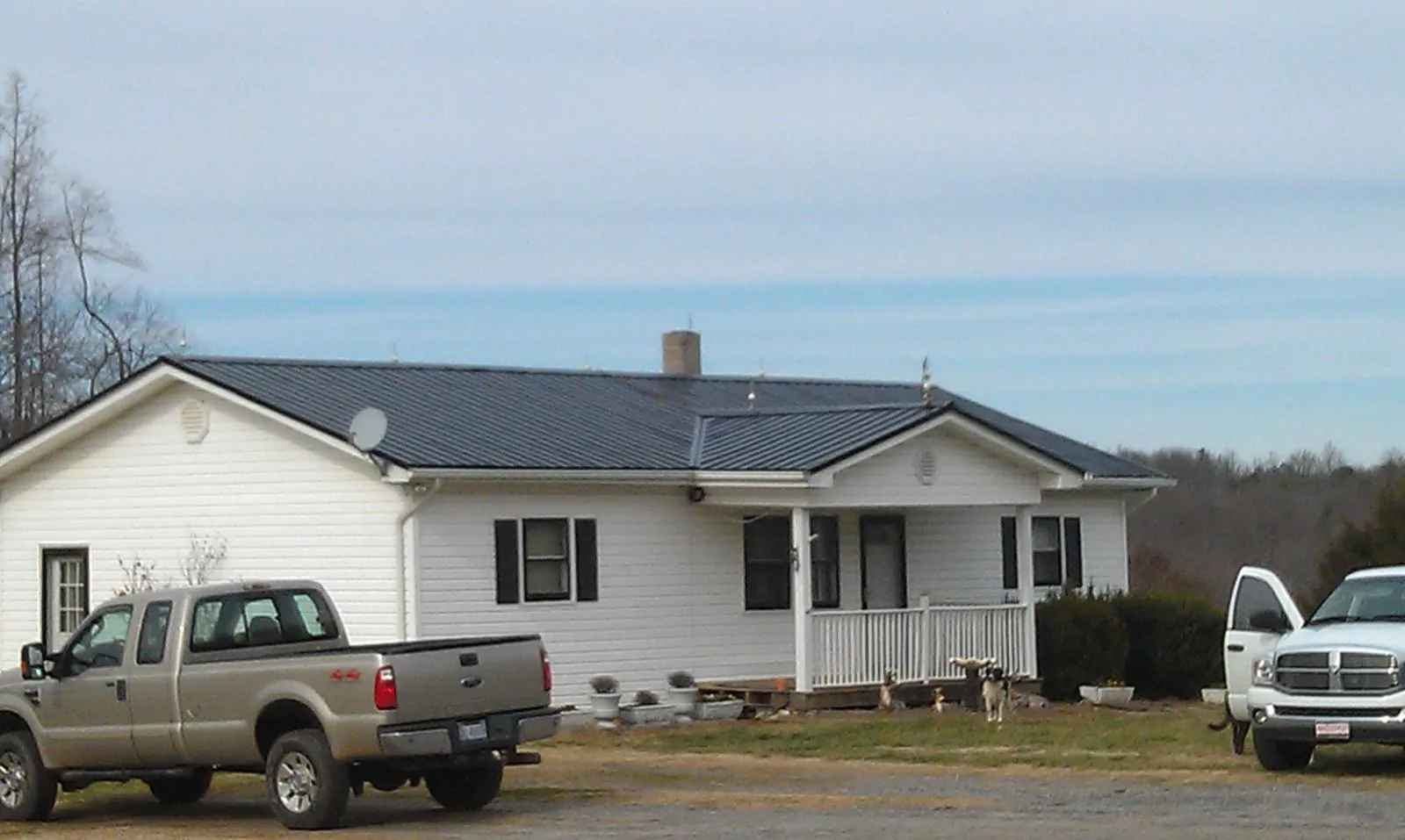 Finished dark metal roof on a white ranch home with work trucks parked in Alcoa