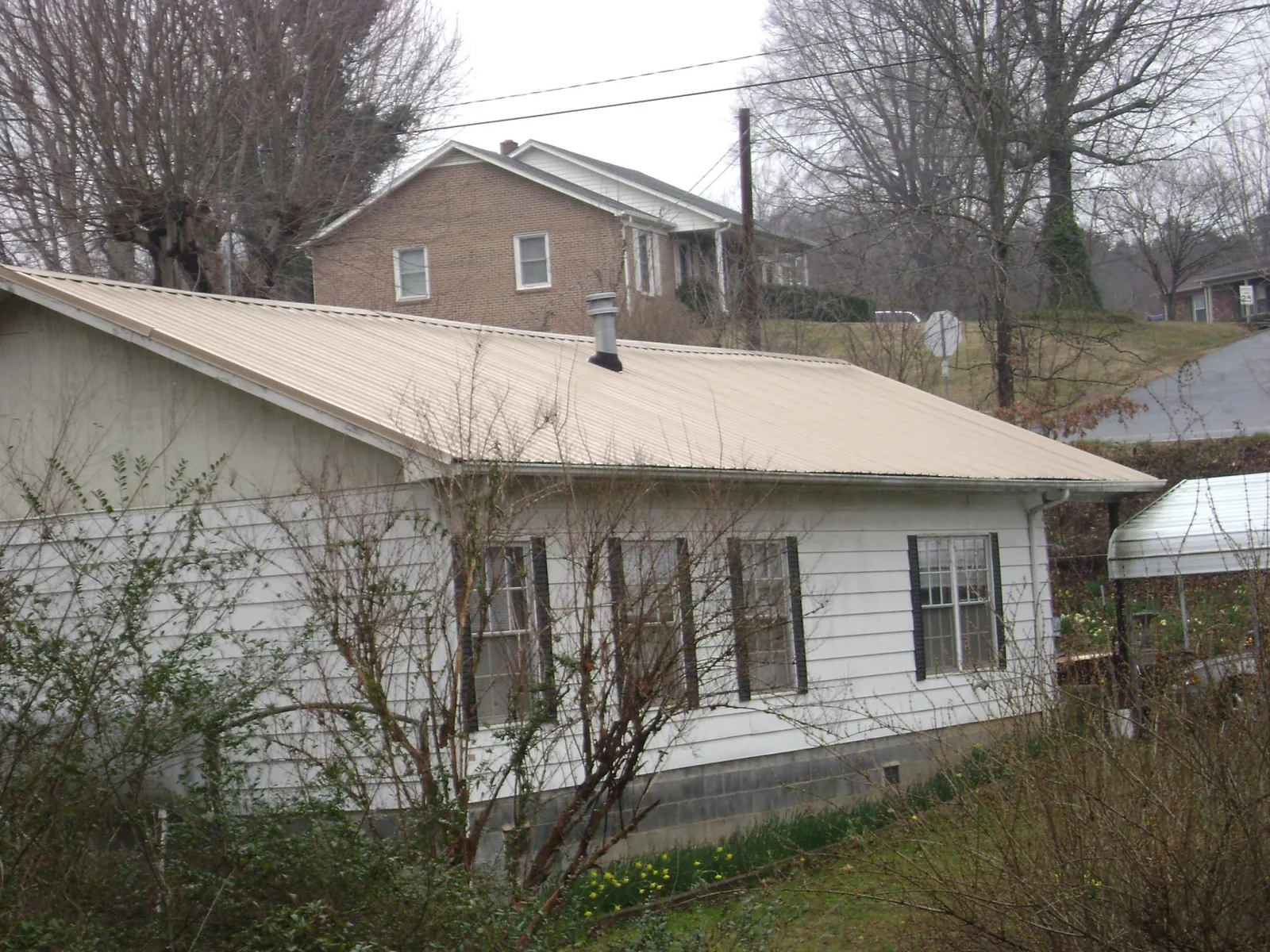 Tan metal roof on a white sided house set into a hillside — Commercial Roofing by Roofing Brothers in Alcoa